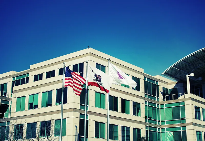 Bâtiment du siège historique d'Apple à Cupertino avec drapeaux américain et californien