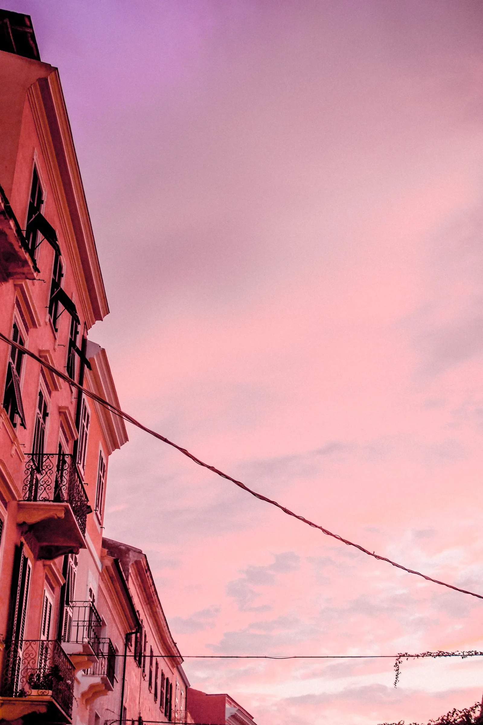 Façades de maisons rouges sous un ciel rose dans une ruelle de La Maddalena
