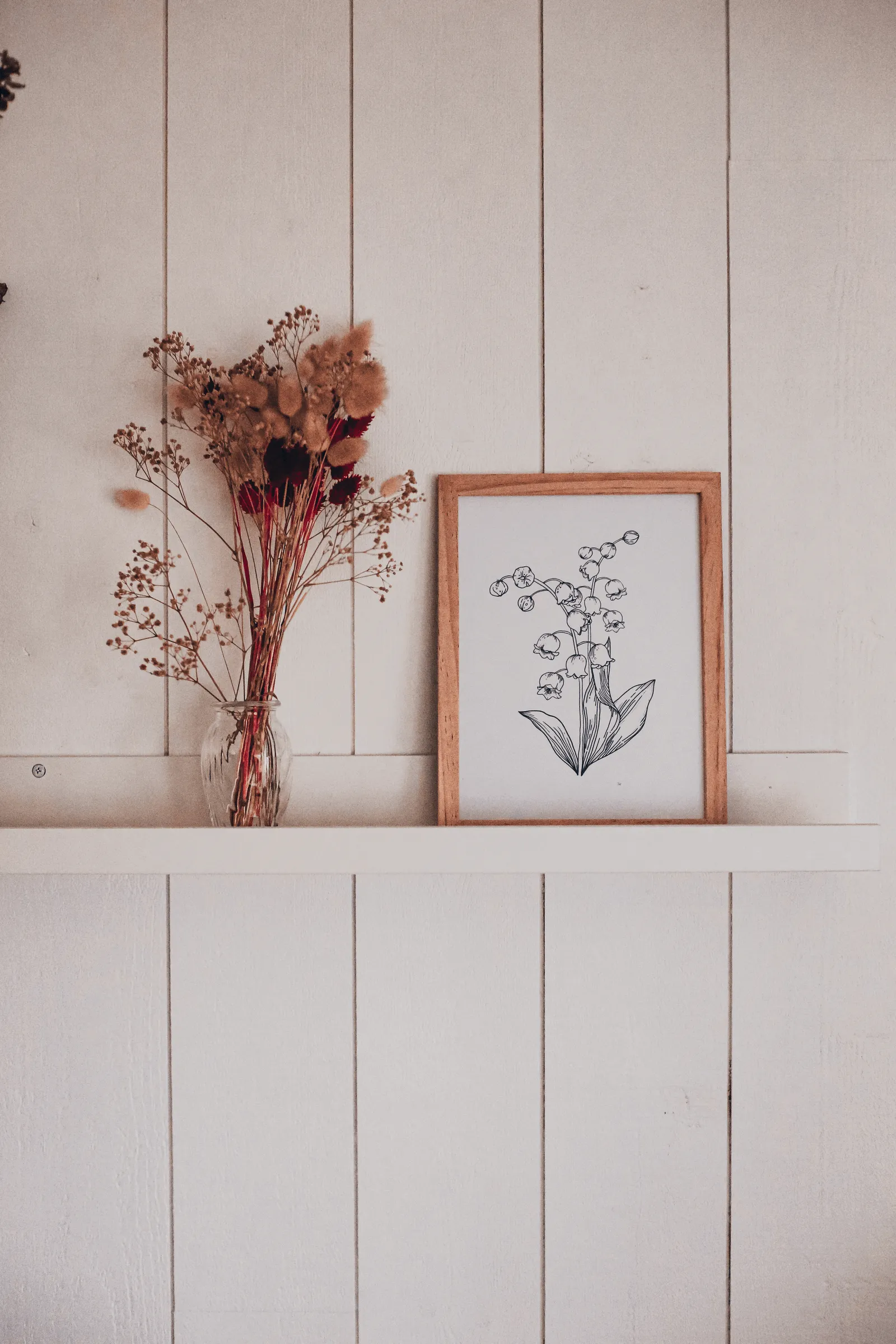 Illustration de muguet encadrée sur une étagère blanche à côté d'un bouquet sec