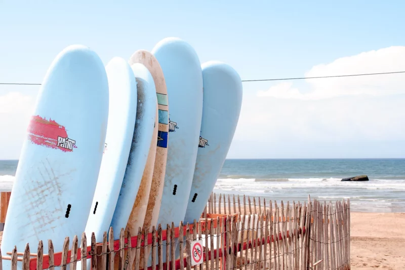 Planches de surf alignées contre une ganivelle face à l'océan sur une plage du Médoc