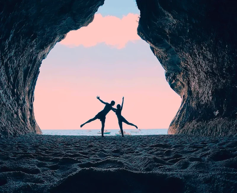 Silhouettes d'un couple dansant à l'entrée d'une grotte face à la mer au coucher du soleil, Cala Gonone