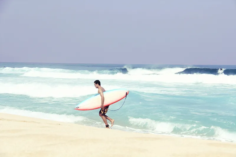 Surfeur sortant des vagues avec sa planche sur une plage de la côte nord d'Oahu