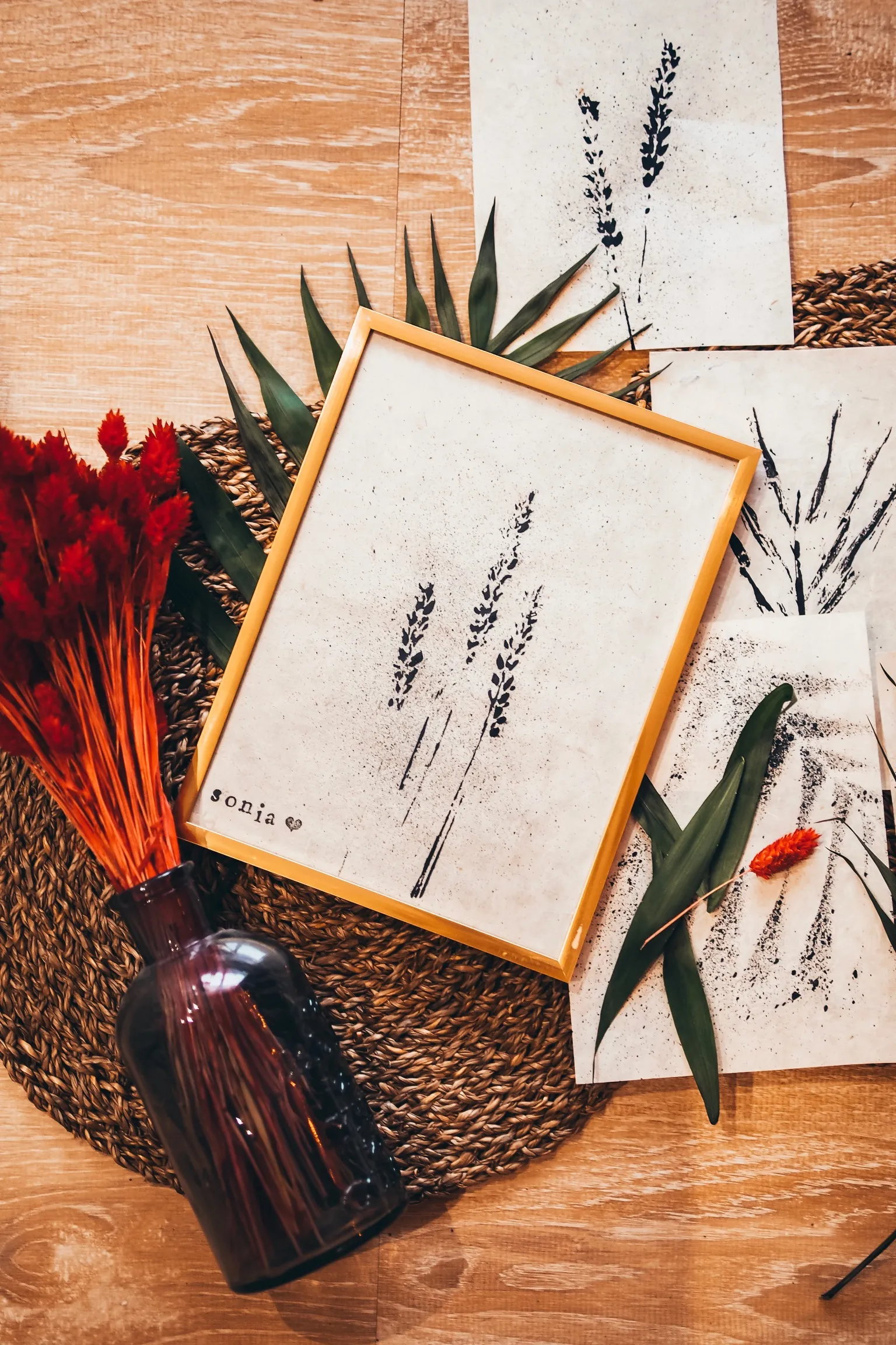 Tableau végétal DIY en cadre doré entouré de fleurs séchées rouges et d'un vase ambré
