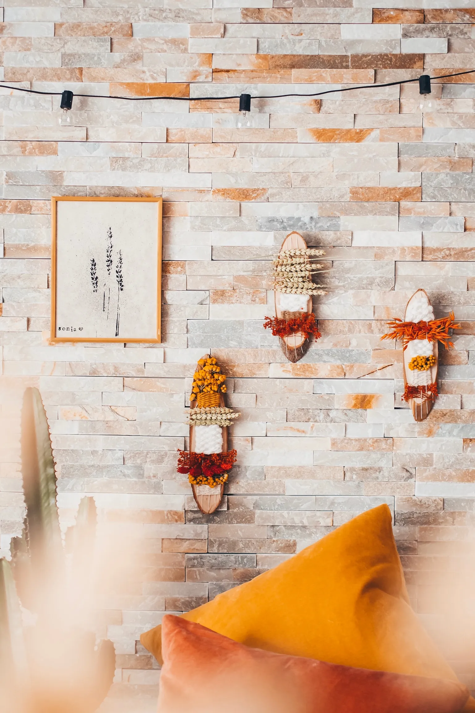 Totems végétaux en fleurs séchées et tableau à empreintes accrochés à un mur en pierre
