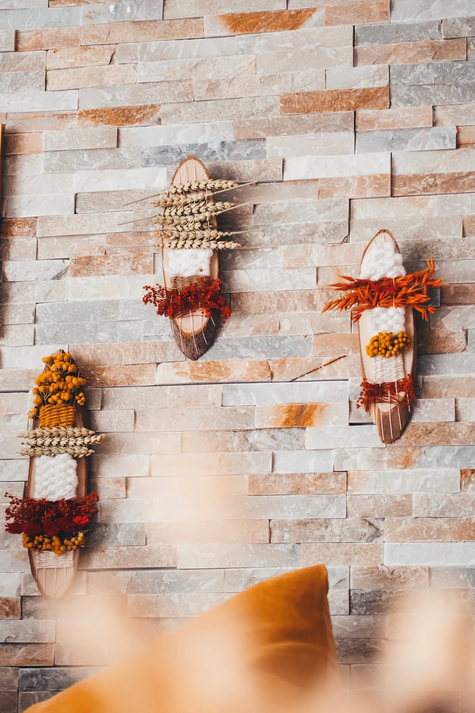 Trois totems végétaux DIY en bois et fleurs séchées accrochés à un mur en parement de pierre