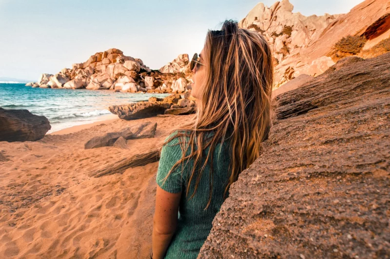 Voyageuse assise sur le sable face aux rochers de granit de Capo Testa en Sardaigne