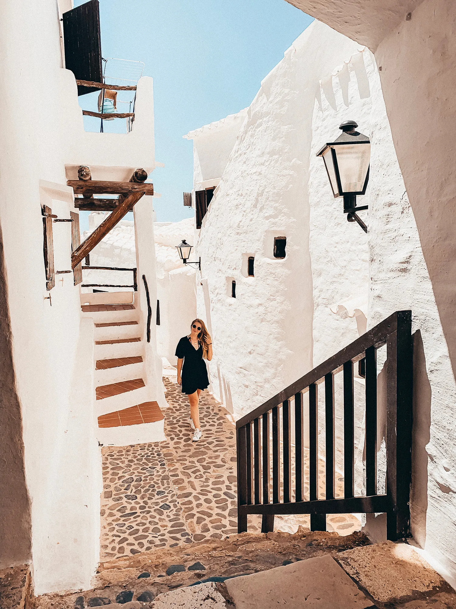 Voyageuse dans une ruelle blanche avec escalier extérieur à Binibeca Vell, Minorque