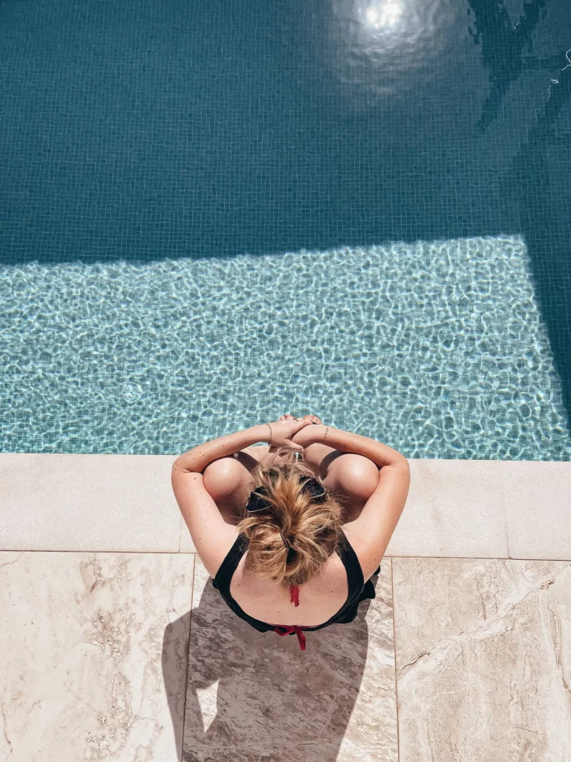 Voyageuse de dos au bord de la piscine au carrelage turquoise du Stella Hotel en Crète